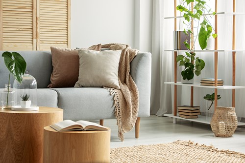 En inredning från ett vardagsrum med soffa, bord, hylla, växt mm i grå, beige, brun och gröna färger.