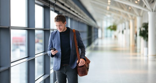 En forretningsmann som skal reise utenlands og ser på mobilen sin mens han går gjennom flyplassen.