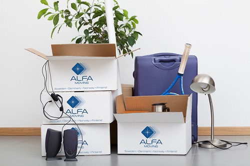 Hvite Alfa-flytteesker med blå Alfa-logoer i en haug sammen med diverse innbo som skal pakkes og plasseres på langtidslager.