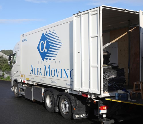 Hvid Alfa-lastbil med blåt Alfa-logo som leverer bohave udenfor et privatejet hjem.