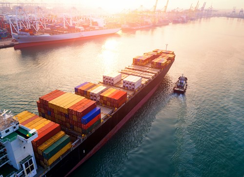 A large shipping vessel for sea freight transporting containers with household goods in the harbour in sunset.