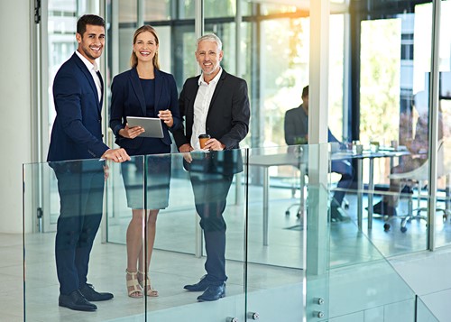 A business office setting with three people standing together at a glass railing.