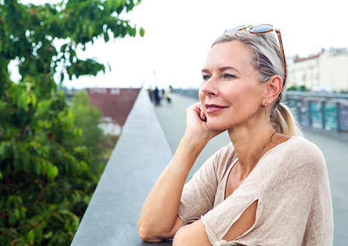 A woman standing outside by a bridge looking out at a view with greenery.