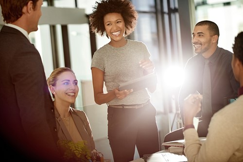 A diverse group of people sitting and standing around a table at an office discussing relocation with a bright light coming from the background.