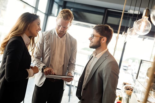 Tre personer interagerer på et kontor og diskuterer import- og eksportpriser.